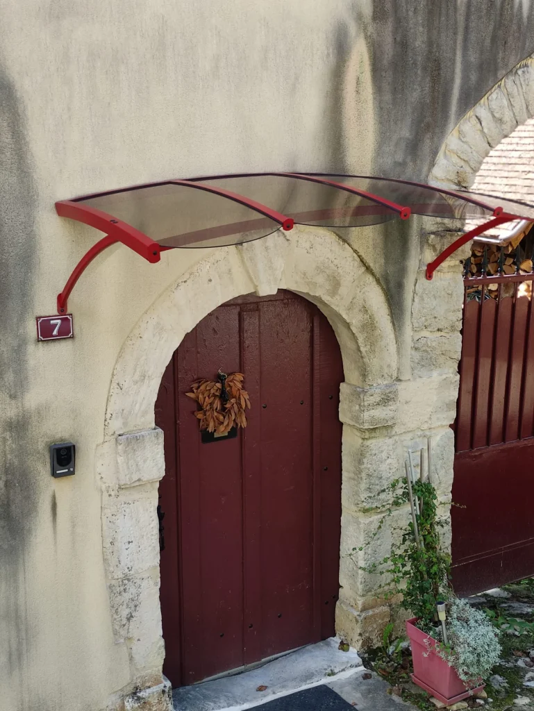 Cet abri de porte d’entrée est en aluminium bombé de couleur rouge, il est muni de polycarbonate teinté bronze de 3mm. Ses deux jambes de force sont cintrées